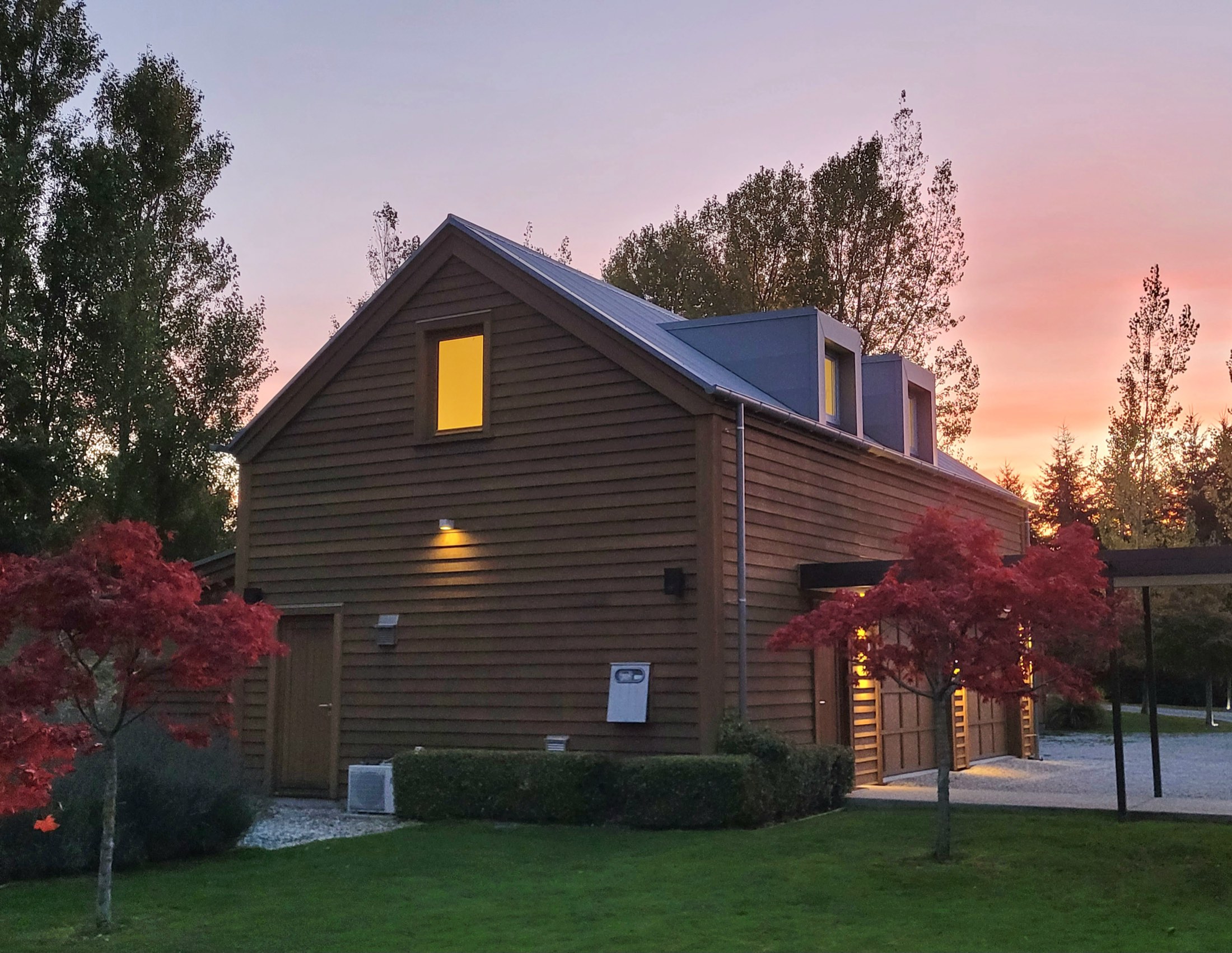 The Loft at Slopehill, a cedar barn with dormer windows lit at sunset behind red maples