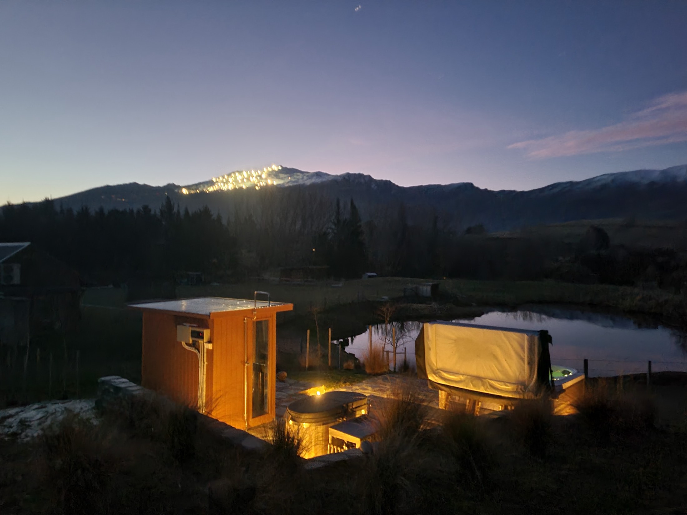 The sauna and spa at dusk, with Coronet Peak lit for night skiing behind